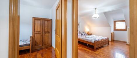 A bedroom with a wooden wardrobe, a bed, and a sloped ceiling with a window.