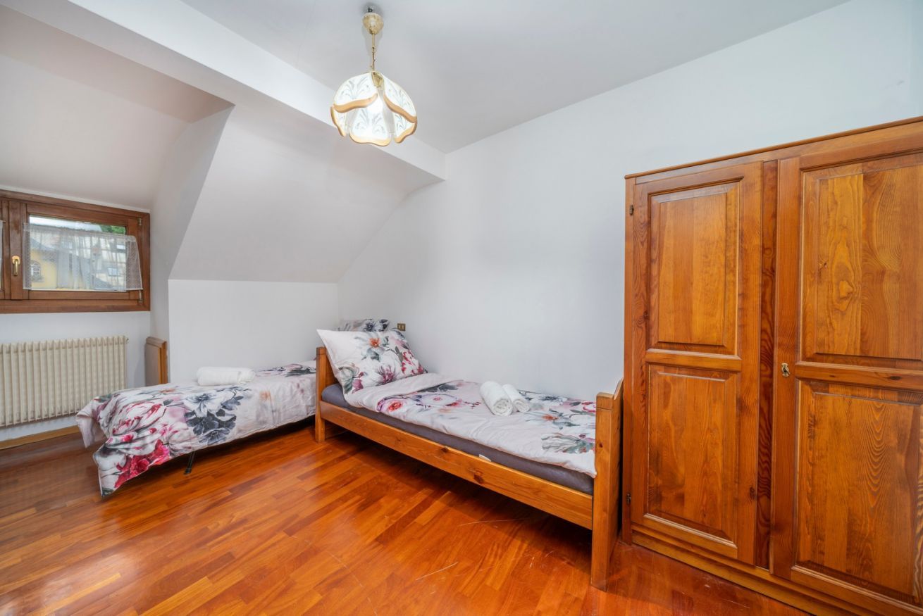 Un dormitorio con un armario de madera, una cama con ropa de cama floral, un radiador y una ventana con persianas.