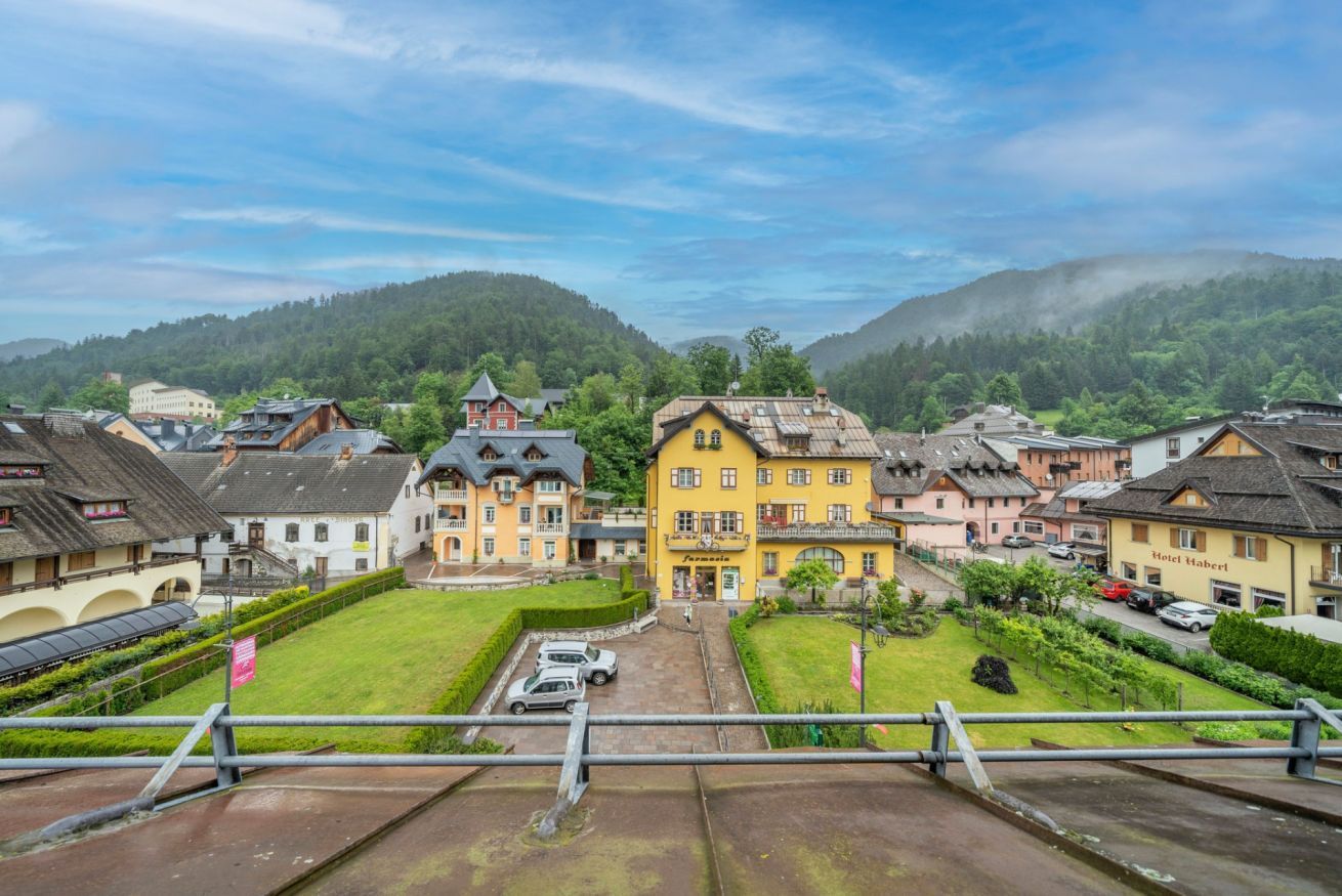 A town with traditional buildings, a central yellow building, and a view of green hills.