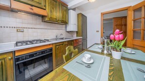 A kitchen with wooden cabinets, a gas stove, a sink, and a dining table with a placemat. - GuestHost - Penthouse Central Apartment (Tarvisio)