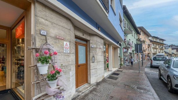 A street view with a building featuring a wooden door, a sign with the number 85, and a flower display outside. - GuestHost - Penthouse Central Apartment (Tarvisio)