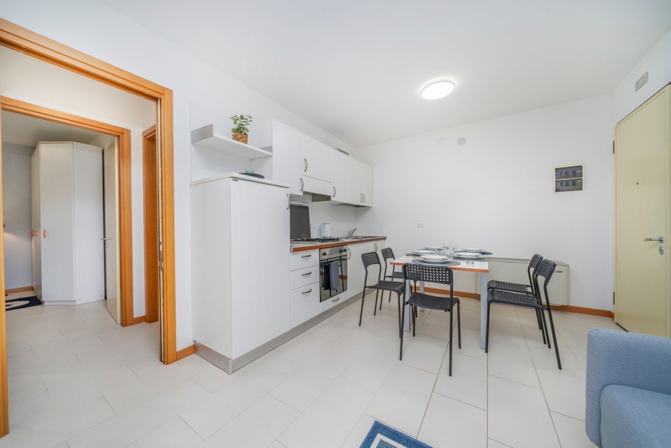 Una cocina compacta con muebles blancos, una mesa de comedor con sillas y un refrigerador pequeño.