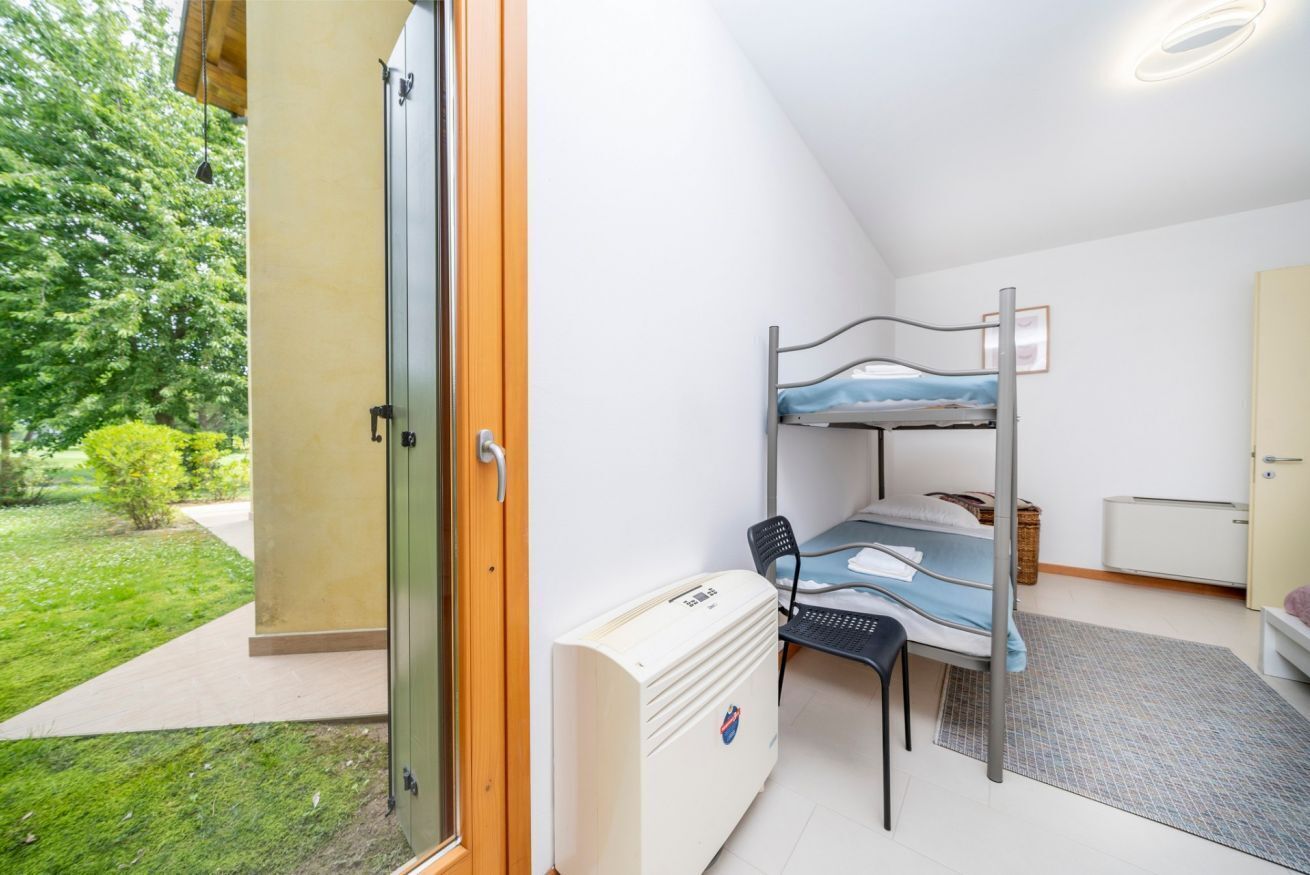 A room with a bunk bed, a desk with a chair, a radiator, and a door leading to a balcony.