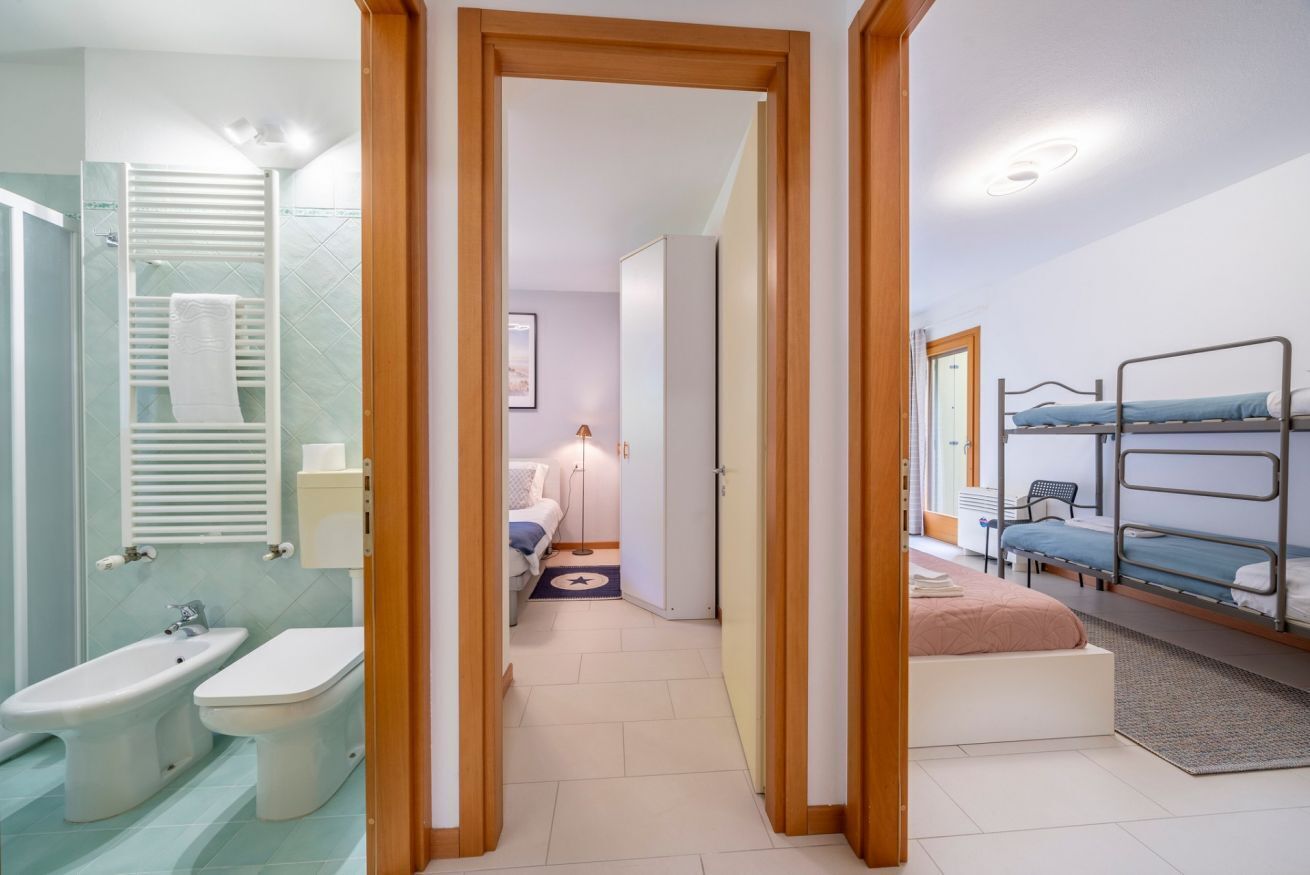 Habitación de hotel con ducha, bidé, cama y literas, con un pasillo que da a un baño.