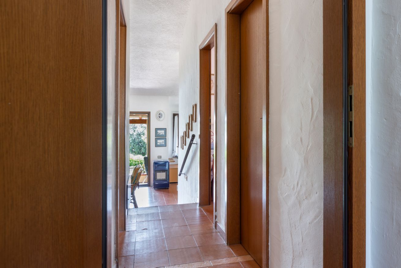 A hallway with wooden doors, a tiled floor, and a view into a room with a window and a heater.