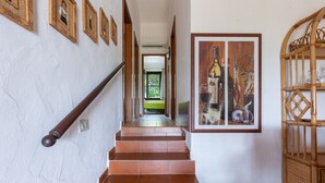 Een trap met een houten leuning, een muur met ingelijste foto’s, en een groot kunstwerk met daarop flessen en glazen.