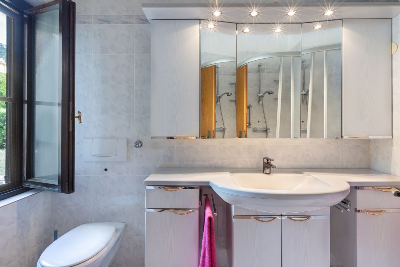 Un baño moderno con inodoro, lavamanos, espejo y ducha.