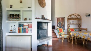 Een woonkamer met een open haard, boekenkasten, een eethoek met rieten stoelen en een trap.