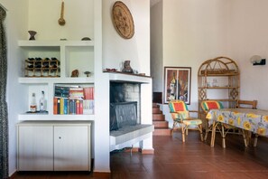 A living room with a fireplace, bookshelves, a dining area with wicker chairs, and a staircase. - GuestHost - Roomy villa of 66sqm located on two levels (stairs to access), can accommodate up to 5 people.The accommodation is located in Costa Rei, area served by all the main services: bars, restaurants, supermarkets and pharmacy. A few steps from the  (Costa Rei)
