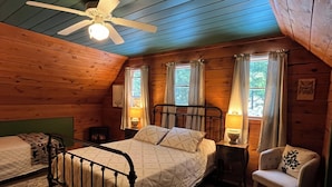 Quarto de cabana aconchegante com uma cama de solteiro, uma cadeira, uma mesa de cabeceira e um ventilador de teto.