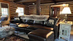 Interno di una baita di legno con un divano in pelle, poggiapiedi e un tappeto decorato.