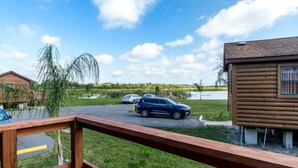 A wooden cabin with a deck, surrounded by a grassy area and a body of water. - Lakefront Cabin #403, 10mins to Beach/Pet Friendly/Prime Location/BOOK TODAY (Seminole)
