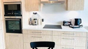 A modern kitchen with wooden cabinets, a built-in oven, a microwave, a coffee maker, and a kettle on the countertop. - Spac. Flat -Kirchberg w Parking&Terrace (Luxembourg City)