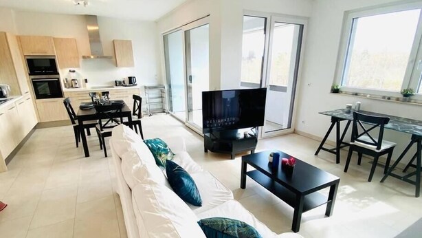 A modern living room with a sofa, TV, and dining area. - Spac. Flat -Kirchberg w Parking&Terrace (Luxembourg City)