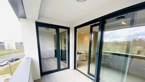 A modern balcony with large glass doors leading to a living area, a tiled floor, and a view of a road and greenery outside. - Spac. Flat -Kirchberg w Parking&Terrace (Luxembourg City)