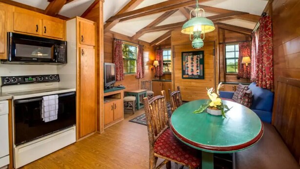 Une cuisine chaleureuse, aménagée dans le style d’un chalet, avec des meubles en bois, un four à micro-ondes et un coin repas doté d’une table et de chaises vertes.