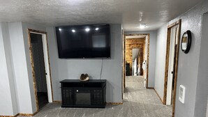 Un pasillo con una televisión de pantalla plana montada en la pared, un mueble multimedia negro con un cuenco decorativo y piso cubierto de alfombra.