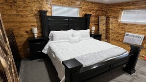 Un dormitorio con paneles de madera en la pared, cabecero negro, colcha blanca y dos lámparas de noche.
