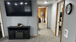 Un pasillo con un televisor de pantalla plana montado en la pared, un mueble de entretenimiento negro con un objeto decorativo y un reloj en la pared.