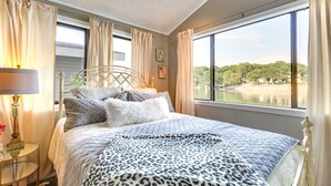 A bedroom with a large window, a bed with a leopard print blanket, and a nightstand with a lamp. - Waterfront Home w/ Dock in South Grand Lake! (Vinita)