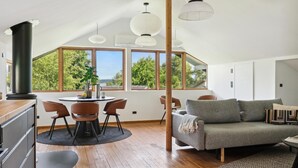 A modern loft with a dining area, a sofa, and large windows offering a view of trees. - 1 bedroom lovely home in Holbæk (Holbæk)