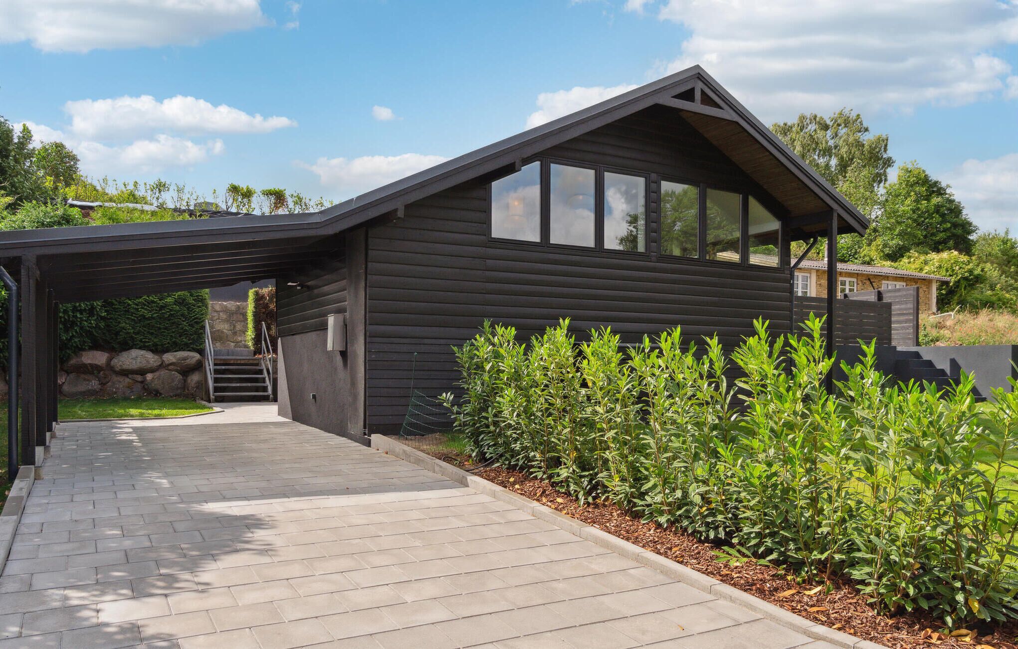 A modern house with a dark wooden exterior, a covered porch, and a paved driveway.
