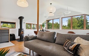 A modern living room with a sofa, a fireplace, and large windows offering a view of the outdoors. - 1 bedroom lovely home in Holbæk (Holbæk)
