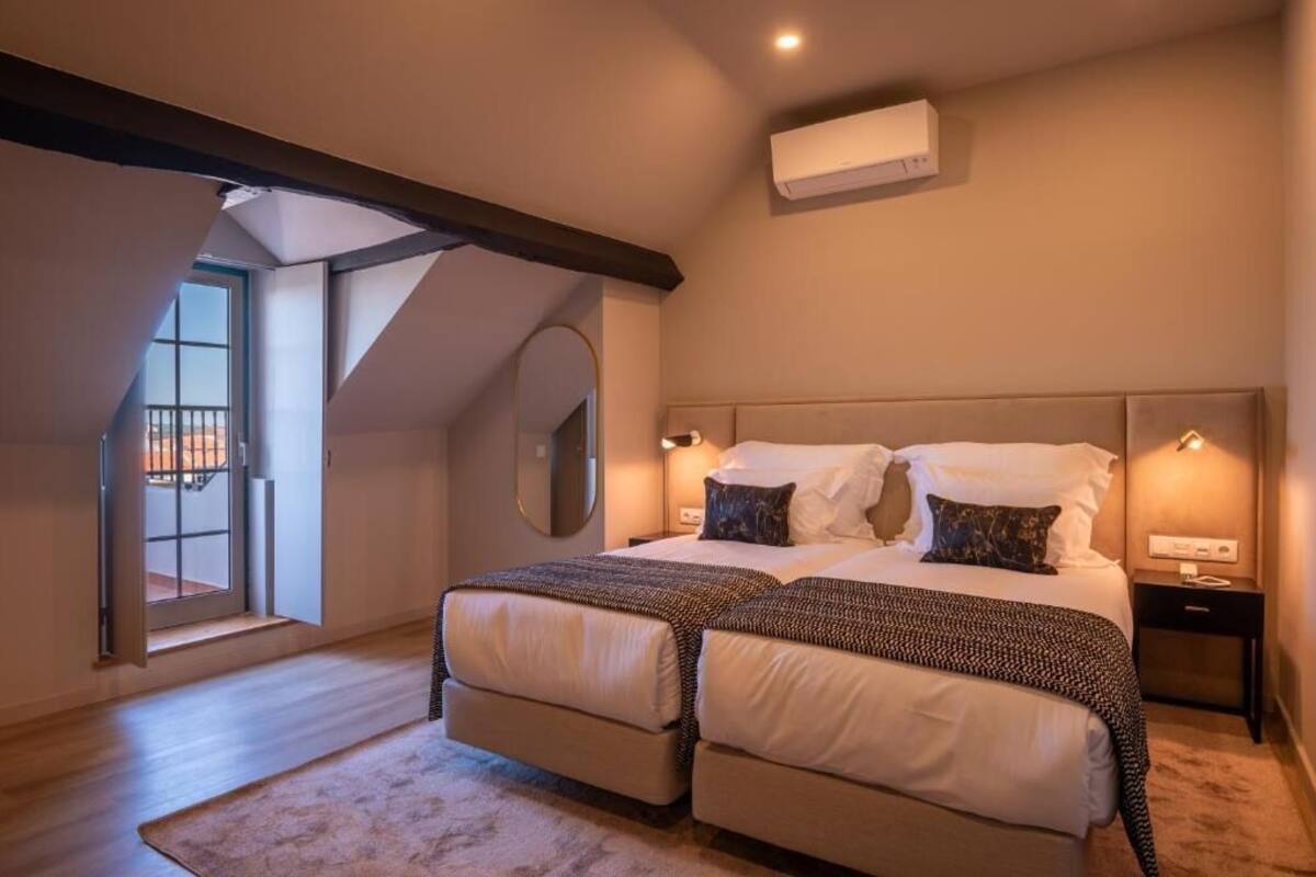 A bedroom with a large bed, two bedside tables, a mirror, and a window with a view.