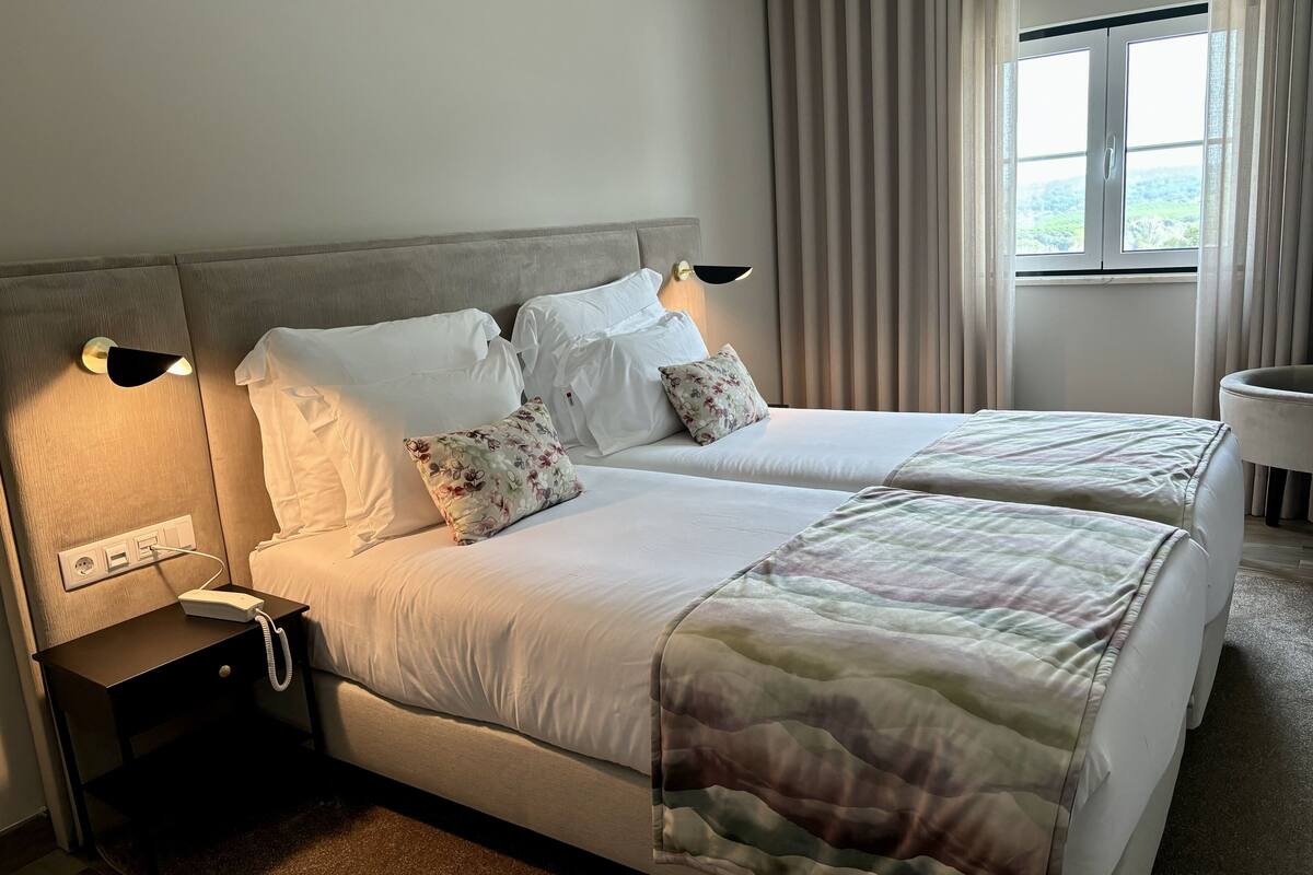 A hotel room with a double bed, bedside tables, a lamp, a phone, and a window with curtains.