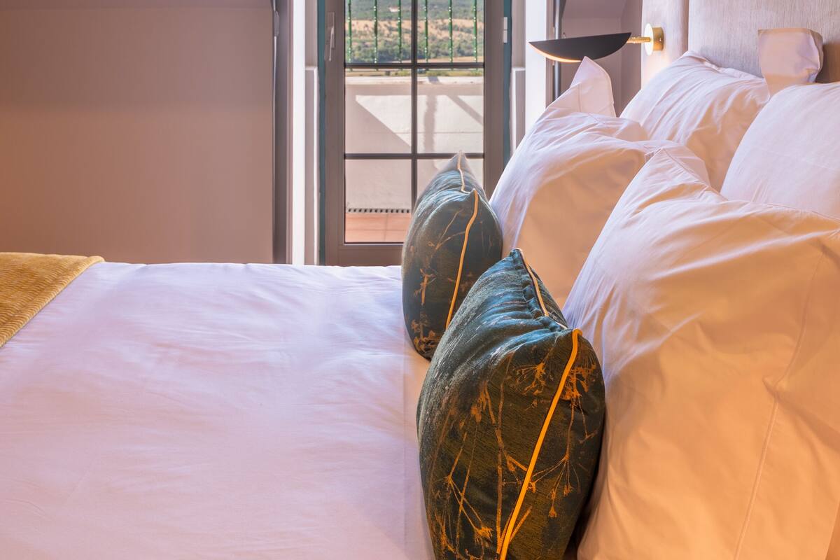 A bedroom with a large bed, a view of the outdoors through a window, and a balcony.