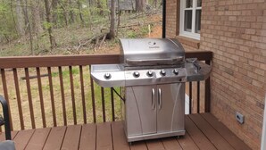 A stainless steel barbecue grill on a wooden deck with a brick wall and a window in the background. - 3 Bedroom House Near Hickory  (Granite Falls)