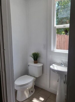 A small, white bathroom with a toilet, a sink, and a window.