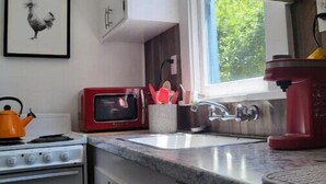 Una cocina con armarios blancos, un microondas rojo, una tetera y un lavabo.