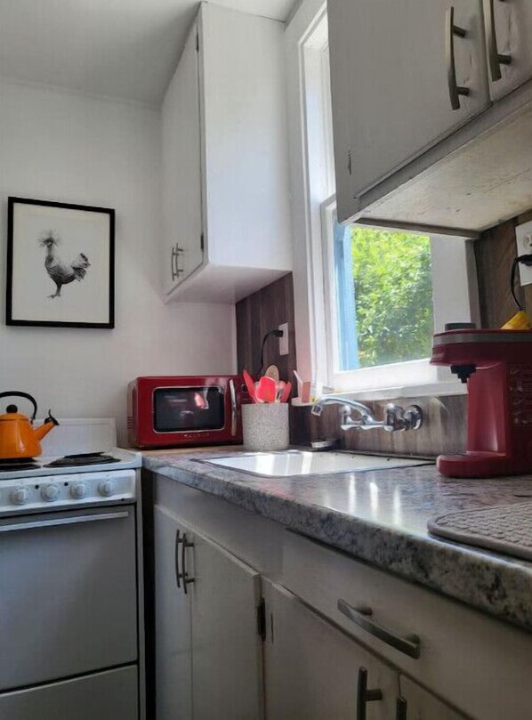 A kitchen with white cabinets, a red microwave, a kettle, and a sink.