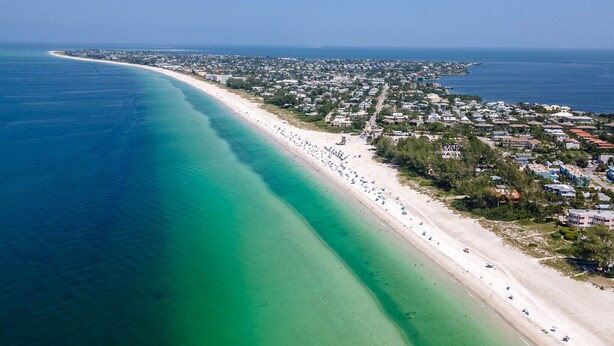 An aerial view of a coastal town with a long, sandy beach and clear turquoise waters.