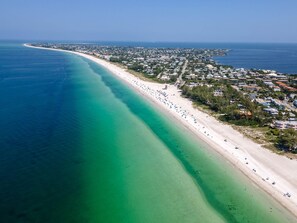 An aerial view of a coastal town with a long, sandy beach and clear turquoise waters. - Beachfront Condo on AMI (Holmes Beach)
