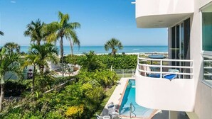 A poolside view with a clear view of the ocean, palm trees, and a white building with balconies.
