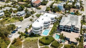 An aerial view of a residential area with a large building featuring a swimming pool, multiple balconies, and a parking area.