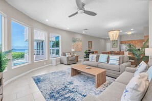 A spacious living room with a large window, a ceiling fan, and a view of the ocean. - Beachfront Condo on AMI (Holmes Beach)