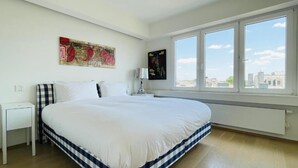 A bedroom with a large bed, a window with a city view, and a ceiling fan.