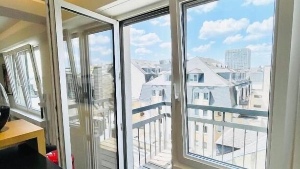 A modern apartment with large sliding glass doors leading to a balcony, offering a view of neighboring buildings.