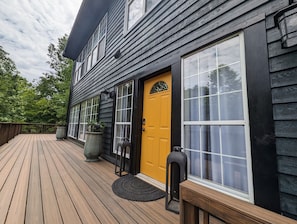 Um deck de madeira com uma porta amarela, janelas grandes e um candeeiro.