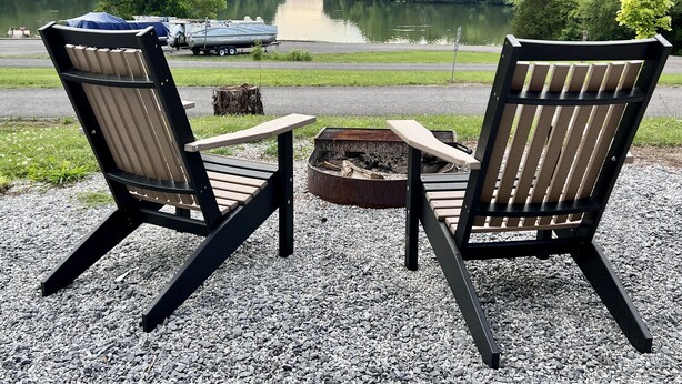 Zwei Adirondack-Stühle, die auf einen See zeigen, mit einem Boot im Hintergrund.
