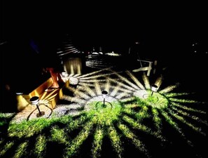 Um espaço exterior escuro com uma instalação luminosa padronizada no chão, possivelmente um elemento decorativo de um jardim ou parque.