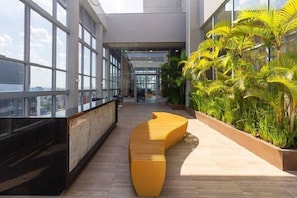 A modern indoor space with large windows, a curved seating area, and indoor plants. - Helbor Wide (São Paulo)