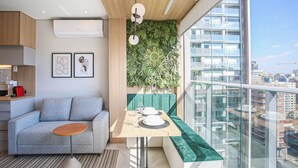 A modern living room with a sofa, a small round table, a bench, and a wall-mounted plant. - Helbor Wide (São Paulo)