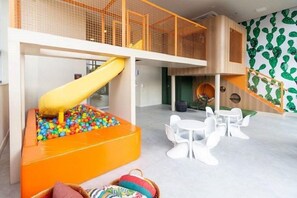A play area with a slide, a ball pit, and a seating area with white chairs. - Helbor Wide (São Paulo)
