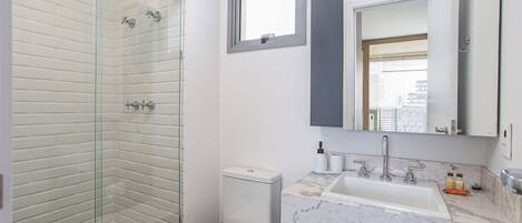 A modern bathroom with a glass shower enclosure, a toilet, a sink with a marble countertop, and a mirror above the sink.
