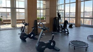 A gym with exercise equipment, large windows, and a view of the city. - Helbor Wide (São Paulo)