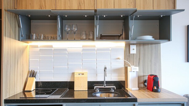 A modern kitchen with a built-in microwave, stove, and sink, along with a coffee machine and utensils. - Helbor Wide (São Paulo)
